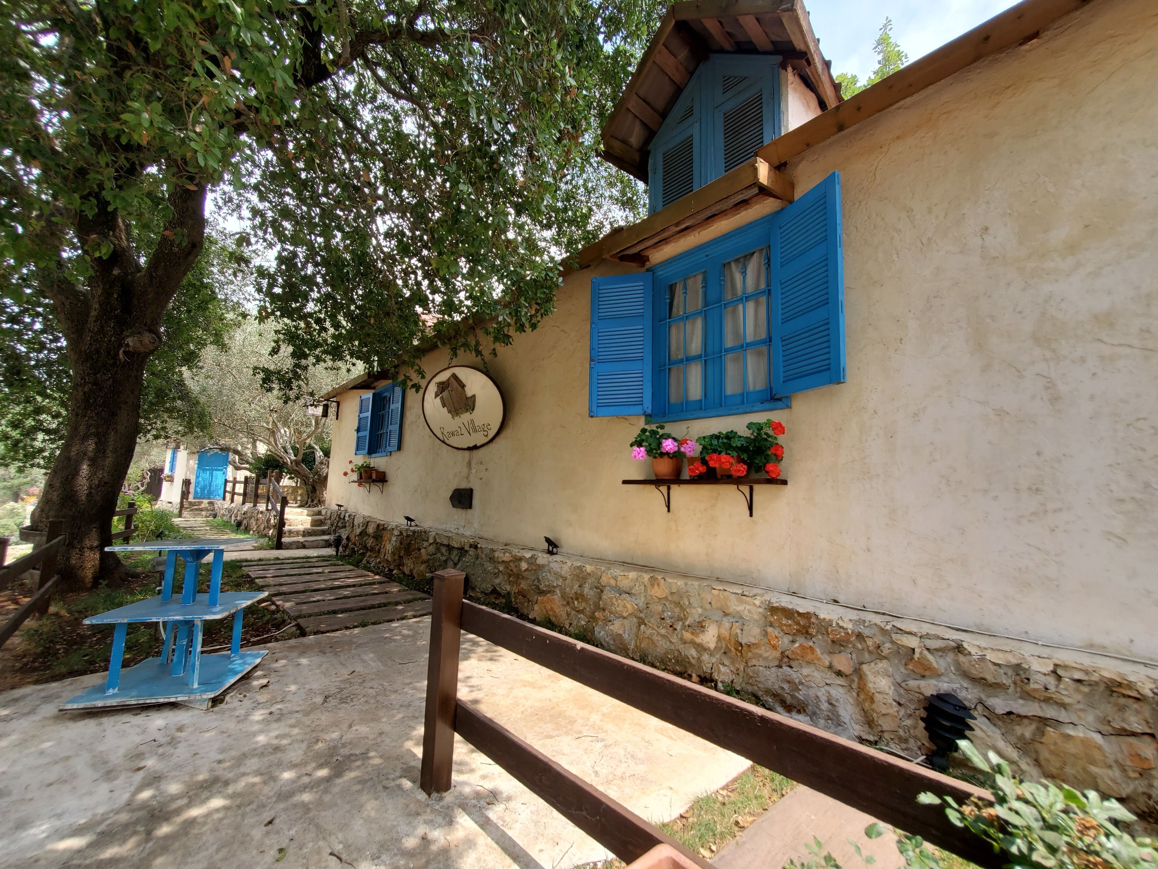 A rustic building with a stone wall, blue shutters, and a sign reading "Ravala Village".