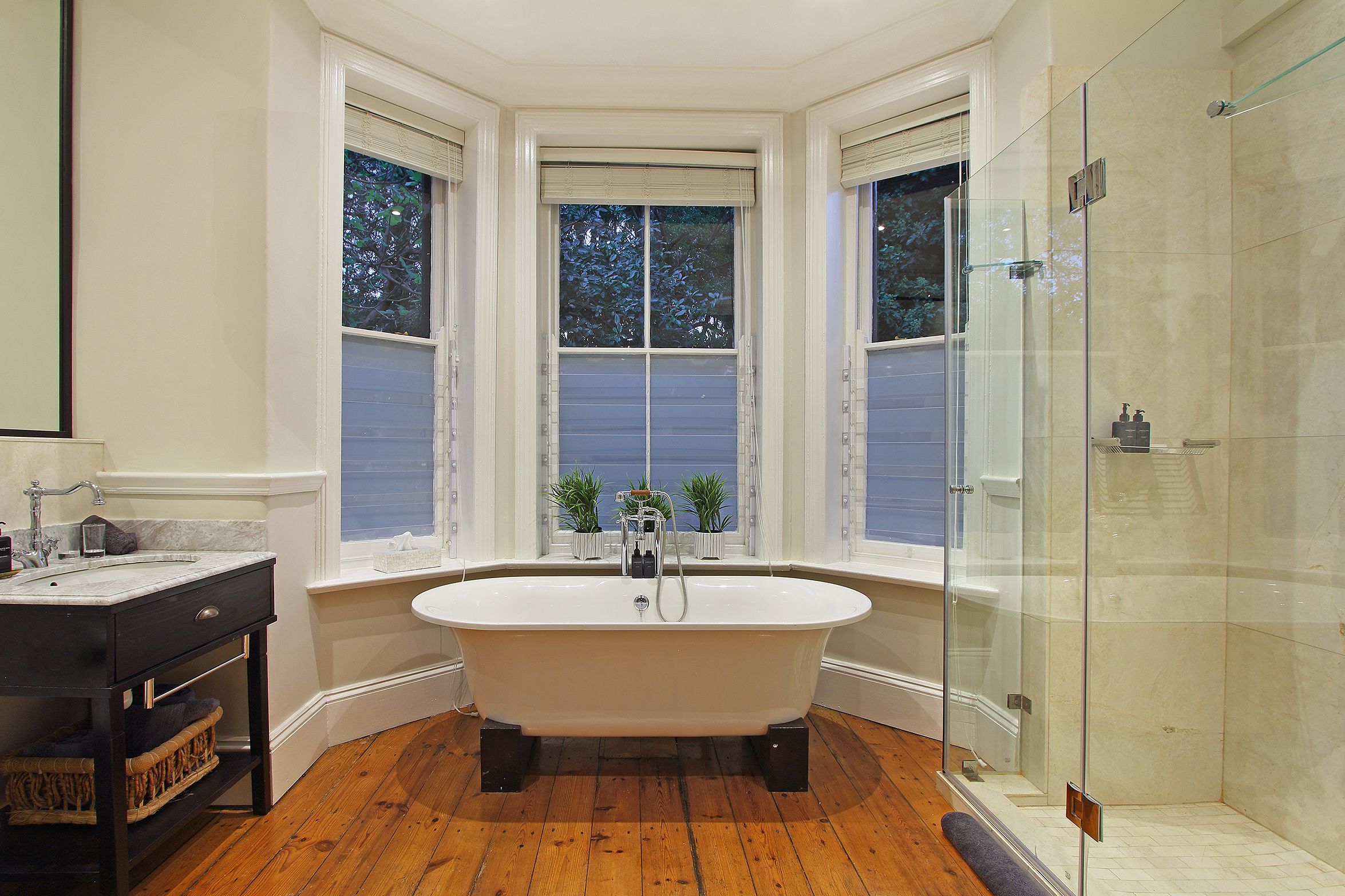 A bathroom with a freestanding bathtub, a glass-enclosed shower, and a window with a view of trees.