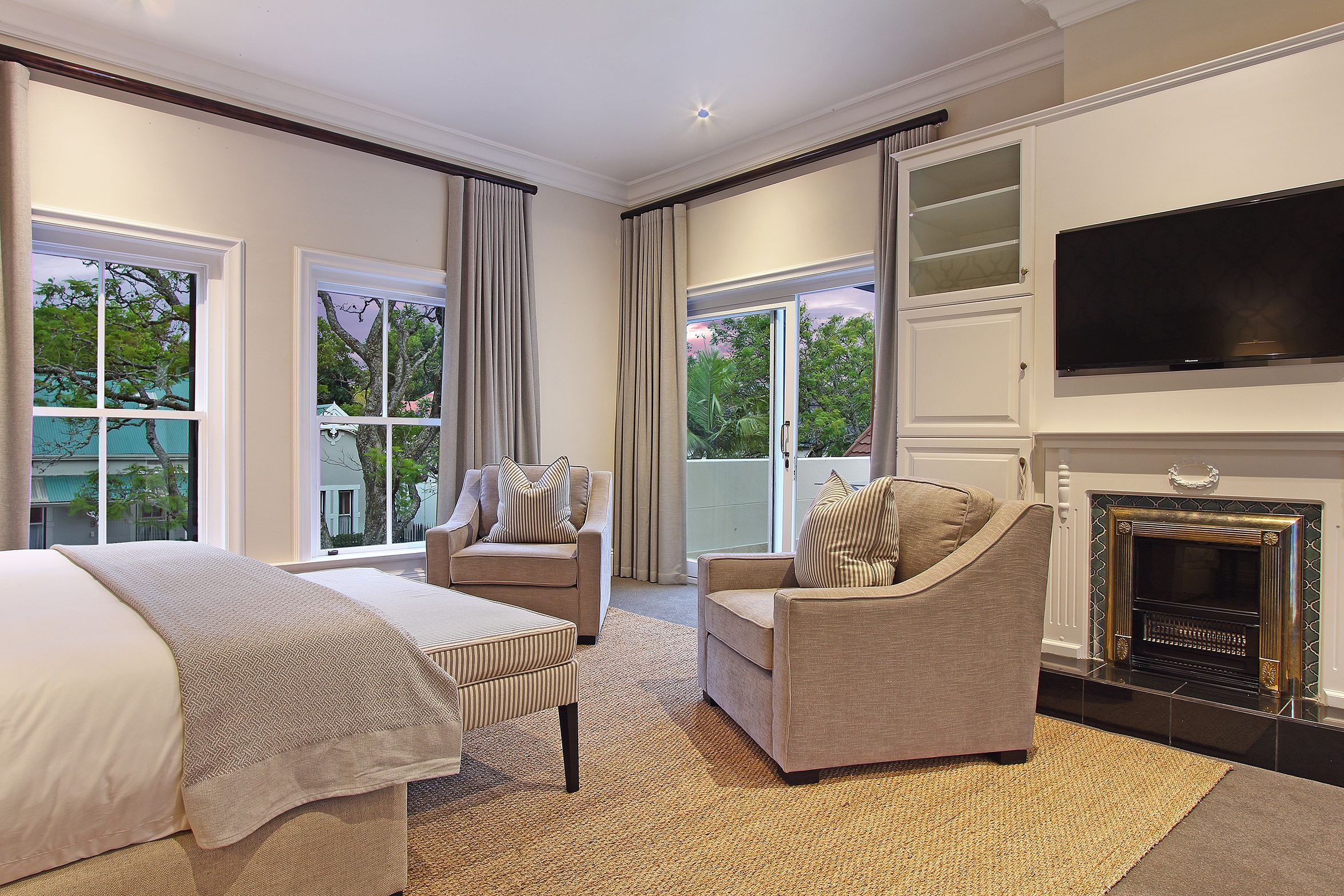 A spacious bedroom with a large bed, two armchairs, a TV, and a fireplace.