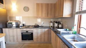 A modern kitchen with wooden cabinets, a built-in oven, and a stainless steel sink. - Ntoma House (Hoedspruit)
