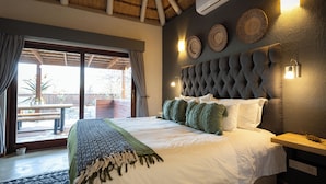 A bedroom with a large bed, a wooden headboard, a nightstand, and a view of the outdoors. - Ntoma House (Hoedspruit)