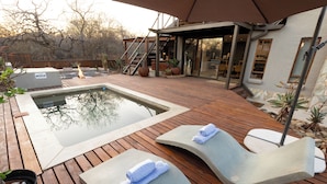A wooden deck with a hot tub, lounge chairs, and a stone wall. - Ntoma House (Hoedspruit)