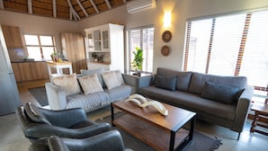 A modern living room with a sofa, armchairs, and a coffee table. There is a kitchen area with cabinets and a dining table. - Ntoma House (Hoedspruit)