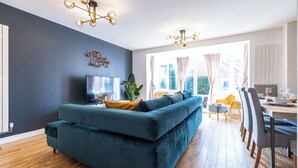 Una sala de estar moderna con un sofá azul turquesa, piso de madera y un comedor con sillas y una mesa.