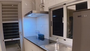 A modern kitchen with white cabinets, a stainless steel sink, and a refrigerator. - Shine Residence (Taichung)