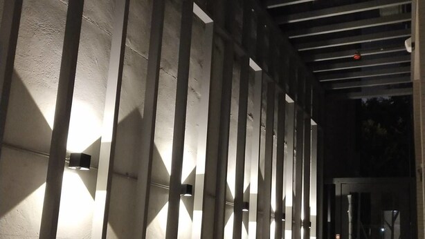 A corridor with a series of vertical beams and illuminated wall panels, leading to a glass door entrance. - Shine Residence (Taichung)