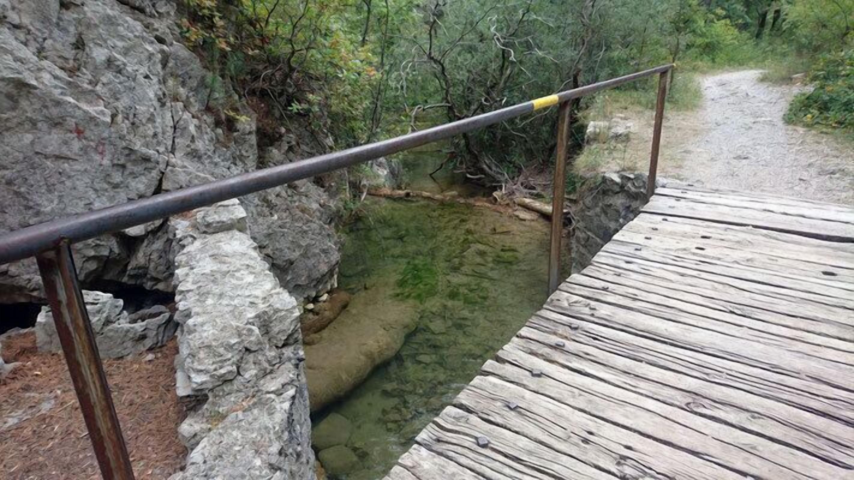 Un puente de madera sobre un arroyo pedregoso, con barandilla metálica.