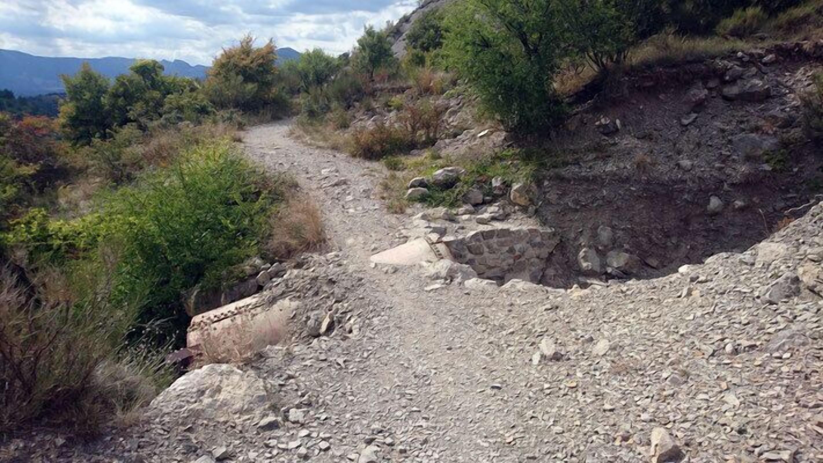 Un sendero pedregoso y accidentado con poca vegetación y una pendiente pronunciada.