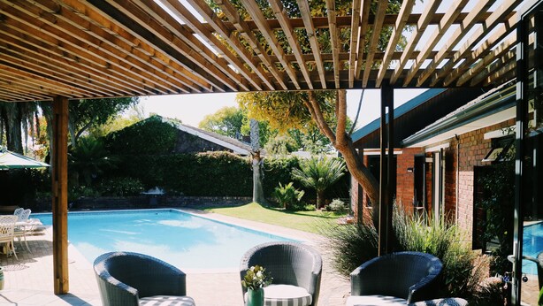 A covered outdoor area with a pool, wicker furniture, and a pergola. - Windsor House (Cape Town)