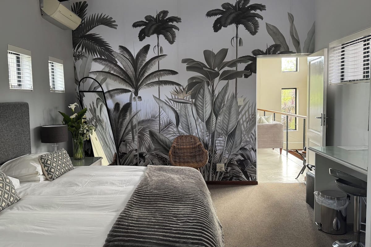 A bedroom with a large bed, a nightstand, a lamp, a wall-mounted TV, and a bathroom with a sink and toilet.