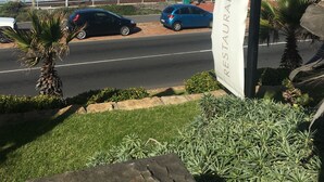A coastal road with a restaurant banner, cars parked along the side, and a view of the ocean. - Windsor House (Cape Town)