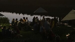 A group of people gathered around a water body at sunset, with a view of a hilly landscape in the background. - Windsor House (Cape Town)