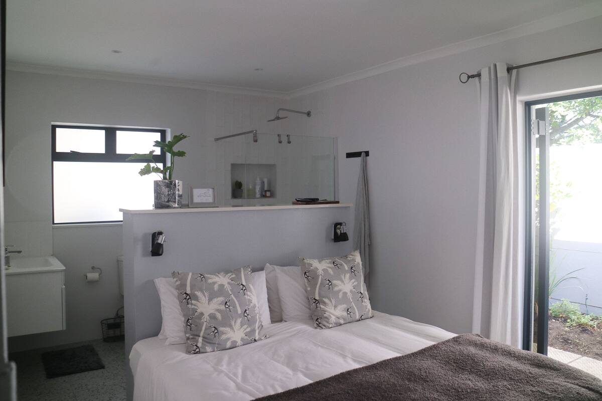 A bedroom with a bed, a window, a shower, and a sink.