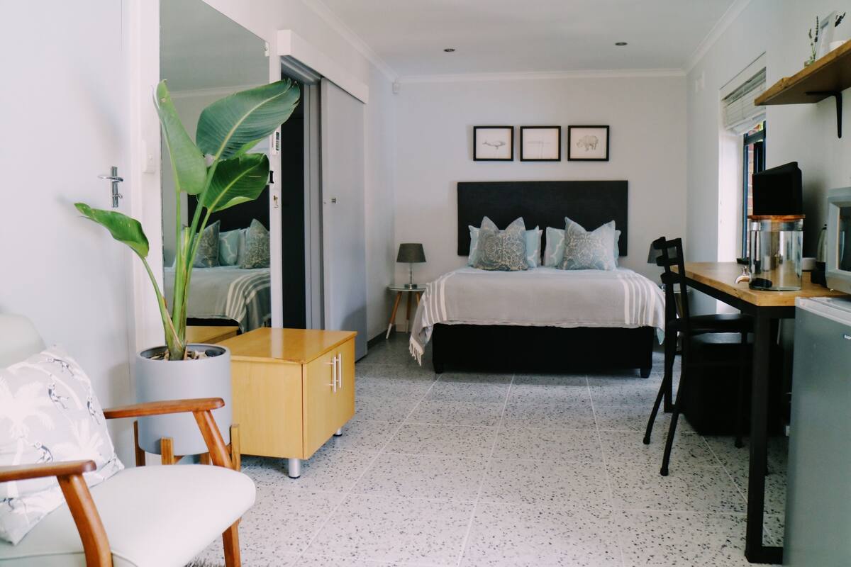A modern bedroom with a bed, bedside table, chair, and a potted plant.