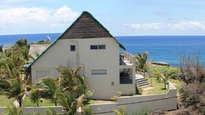 A white building with a green roof, a balcony, and a view of the ocean. - Casa Malcampo (Inhambane)