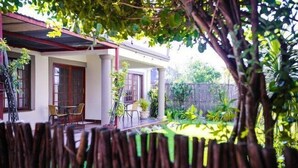 Une maison dotée d’un porche abrité, d’un coin repas avec des chaises et d’un jardin où poussent différentes espèces de plantes.