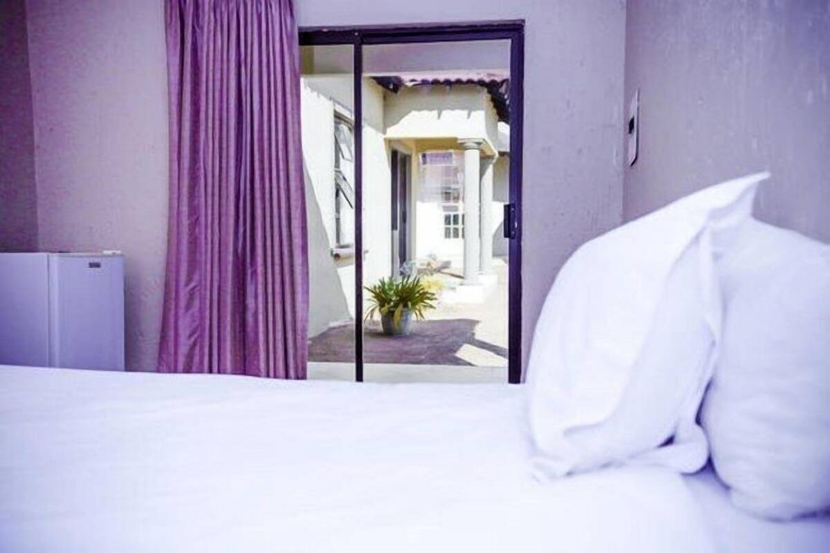 Une chambre avec un lit, une porte-fenêtre coulissante donnant sur un balcon et une plante en pot à l’extérieur.