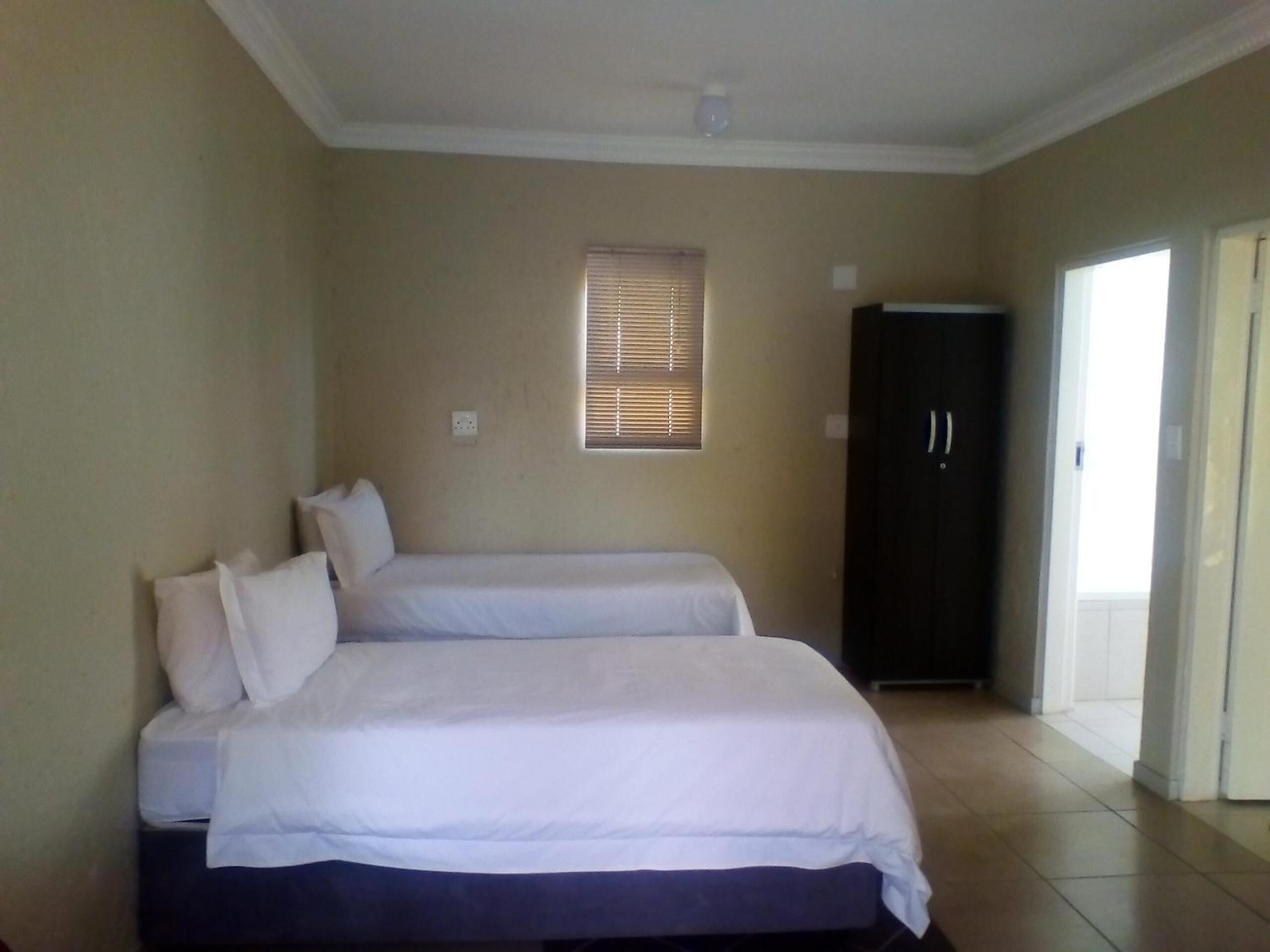 A room with two beds, a wardrobe, and a window with blinds.