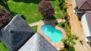 Une piscine entourée d’une terrasse en pierre, avec une pelouse et quelques arbres.