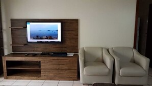 Ein modernes Wohnzimmer mit einer Holz-Unterhaltungseinheit, einem Flachbildfernseher, zwei beigefarbenen Sesseln und einem Couchtisch.