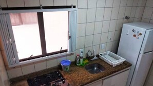 Eine kleine Küche mit einem Gasherd, einem Spülbecken, einem Kühlschrank und einem Fenster mit Jalousien.