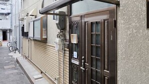 Une rue étroite en milieu urbain, bordée d’un immeuble qui se distingue par une grande porte en bois sombre et un auvent en métal.