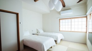 Une chambre d’hôtel minimaliste avec deux lits, une grande fenêtre et un sol recouvert de tatamis, des nattes traditionnelles japonaises.