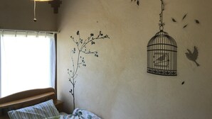 A bedroom with a bed, a hanging light fixture, and wall art including a birdcage and a branch with leaves. - Airfield hill and patchwork hill valley house (旭川市)