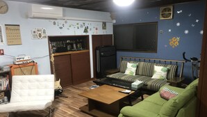 A living room with a sofa, a chair, a coffee table, a TV, and a small cabinet. - Airfield hill and patchwork hill valley house (旭川市)