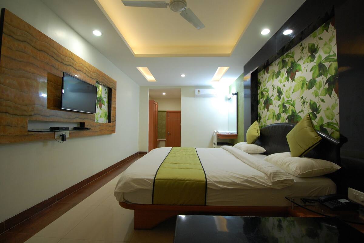 Una habitación de hotel con una cama, un televisor en la pared, un ventilador de techo y una mesita.