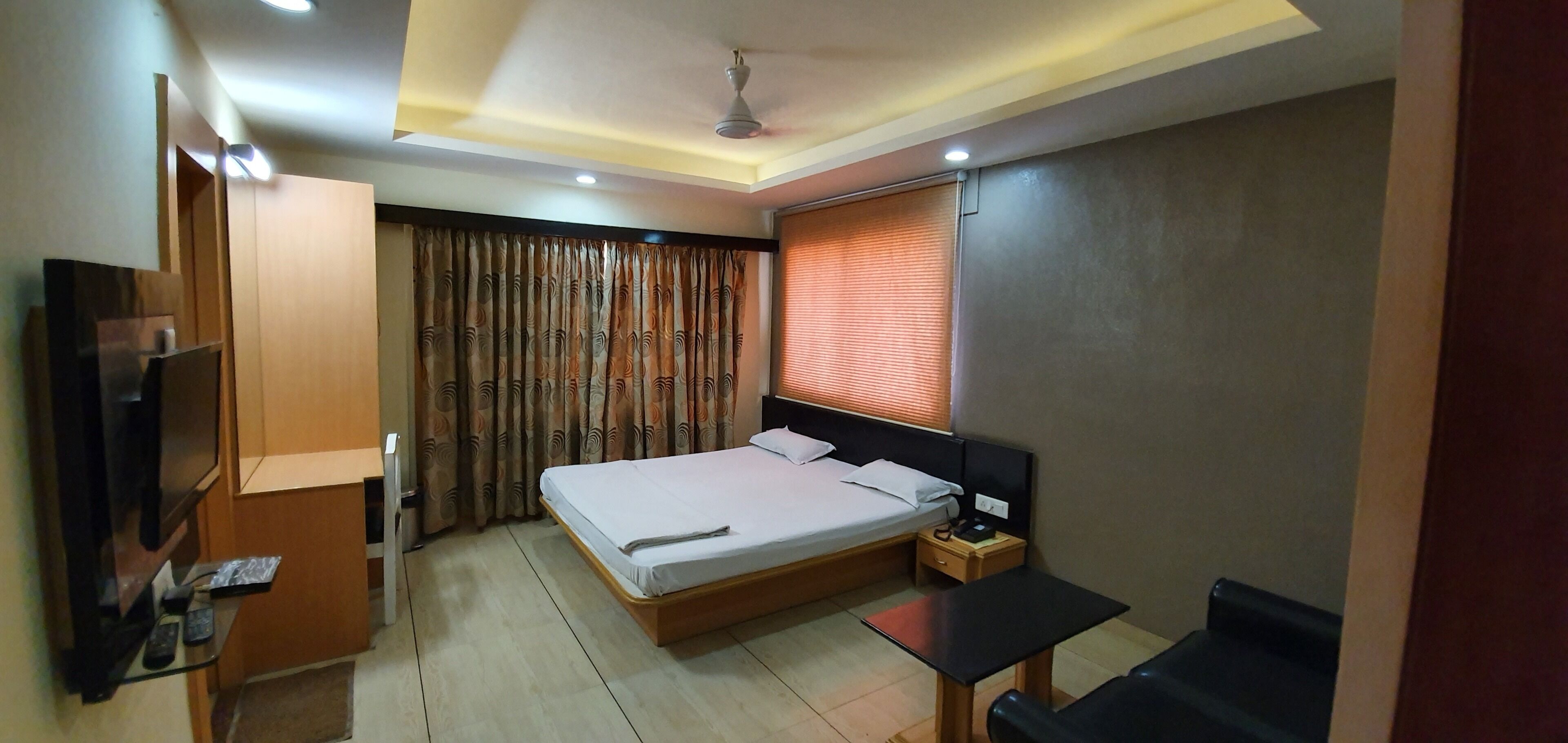 A hotel room with a bed, a desk, a TV, and a ceiling fan.