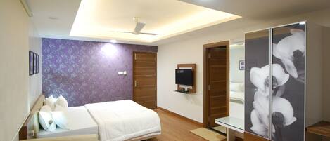 A hotel room with a bed, a bench, a TV, a wardrobe, and a ceiling fan.