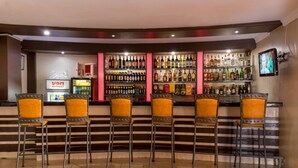 Uma área de bar com cinco banquetas e diversas garrafas de bebidas alcoólicas nas prateleiras.