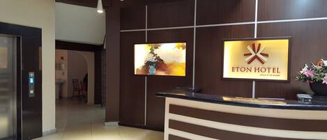 A hotel reception area with a modern design, featuring a reception desk, a mounted television, and a sign for the Eton Hotel.