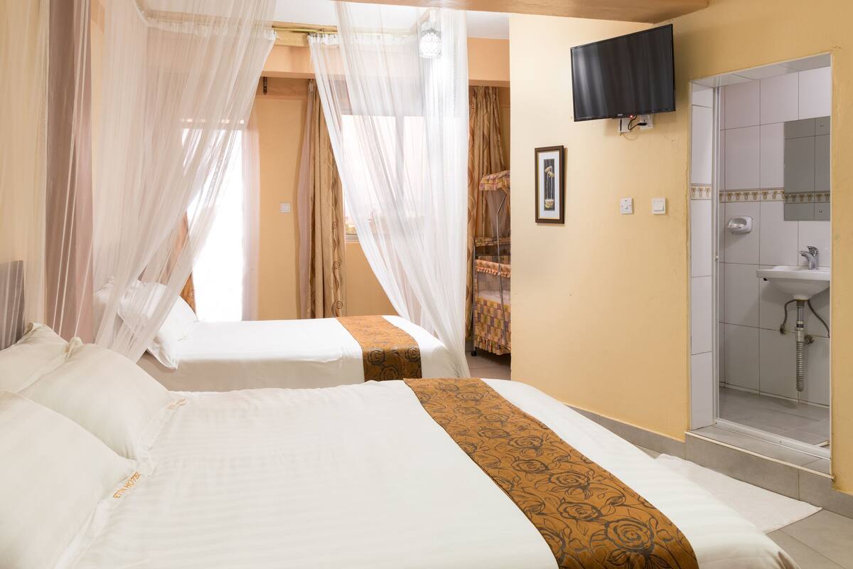 A hotel room with two beds, a shower, a television, and a window with curtains.