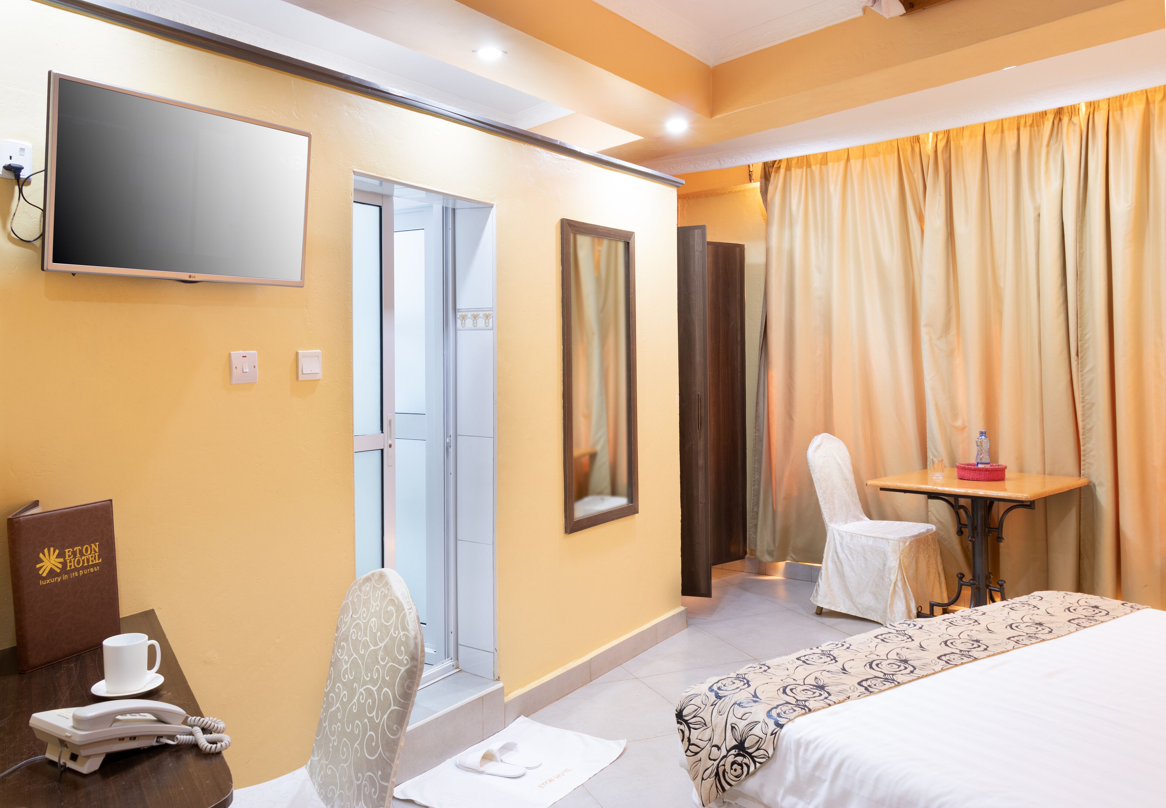 Une chambre d’hôtel avec un lit, un bureau avec un téléphone, une chaise, une table avec une bouteille et un téléviseur fixé au mur.