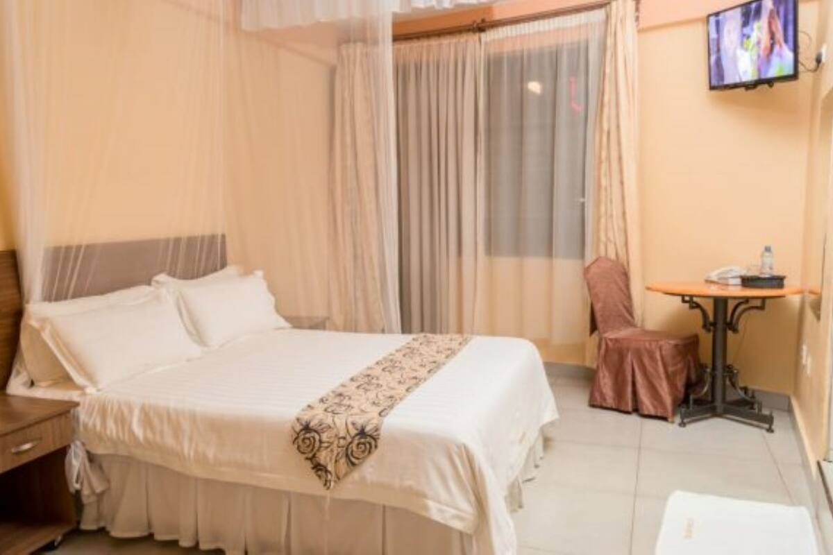 A hotel room with a bed, a nightstand, a table with a chair, and a TV on the wall.