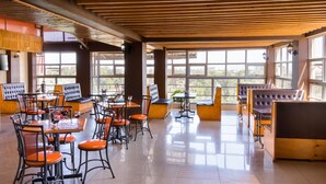Um restaurante amplo com pé-direito alto, grandes janelas e uma variedade de assentos, incluindo mesas e cabines.