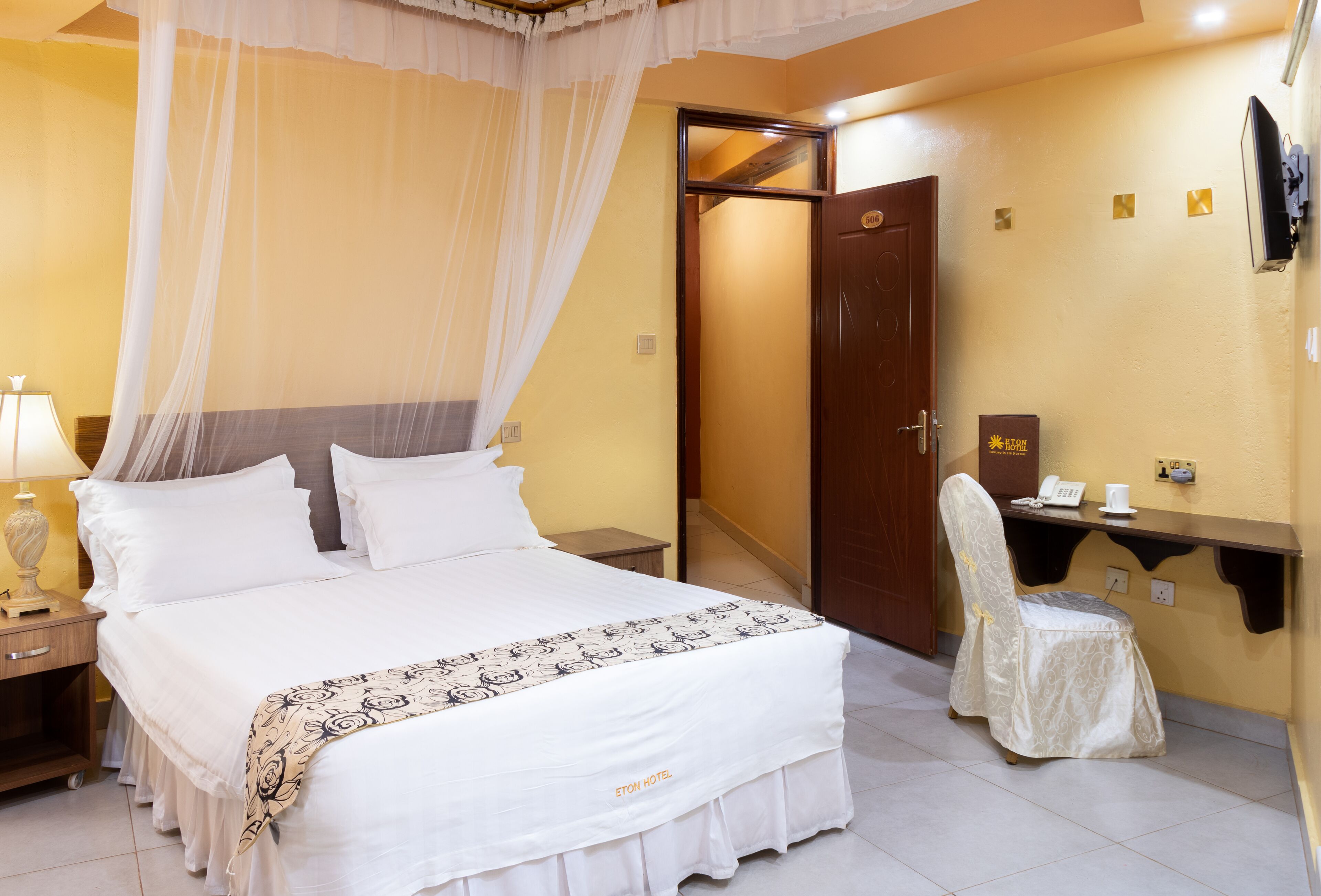 A hotel room with a bed, a nightstand, a chair, a desk, and a door.