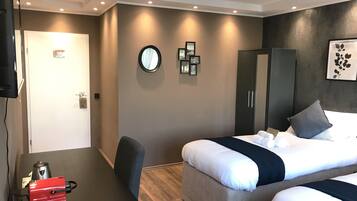 Una habitación de hotel moderna con una cama, un escritorio con un electrodoméstico rojo, un armario y un espejo en la pared.