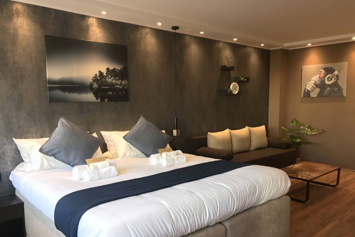 Quarto de hotel moderno com uma cama grande, um sofá e um relógio fixado na parede.