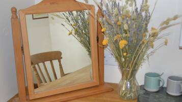 A wooden-framed mirror on a wooden floor, a vase with dried flowers, and two ceramic mugs.