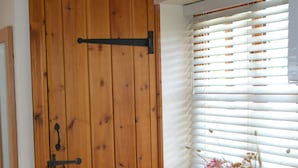 Eine Holztür mit schwarzem Griff, ein Fenster mit weißen Jalousien und eine Vase mit Blumen auf einem Tisch.
