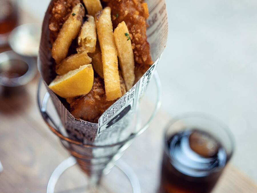 A meal of fried fish and fries served in a paper cone on a wooden table.