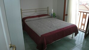 A single bed with a metal frame, a red and white bedspread, and a green lamp on a bedside table.