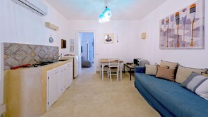 A compact kitchen with a dining area, a blue sofa, and a ceiling light fixture. - La Naca sul Mare (Nardò)