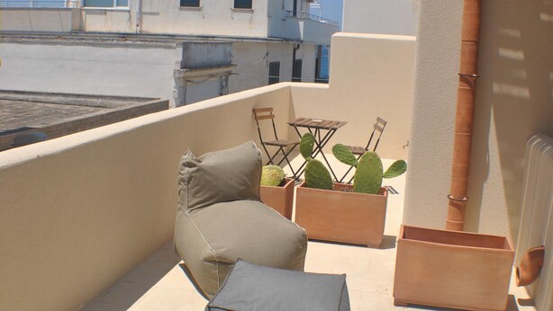 A balcony with outdoor furniture, potted plants, and a view of buildings in the background. - La Naca sul Mare (Nardò)