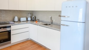 Een moderne keuken met witte kasten, een granieten aanrecht, een ingebouwde oven, een witte koelkast en een achterwand van baksteen.