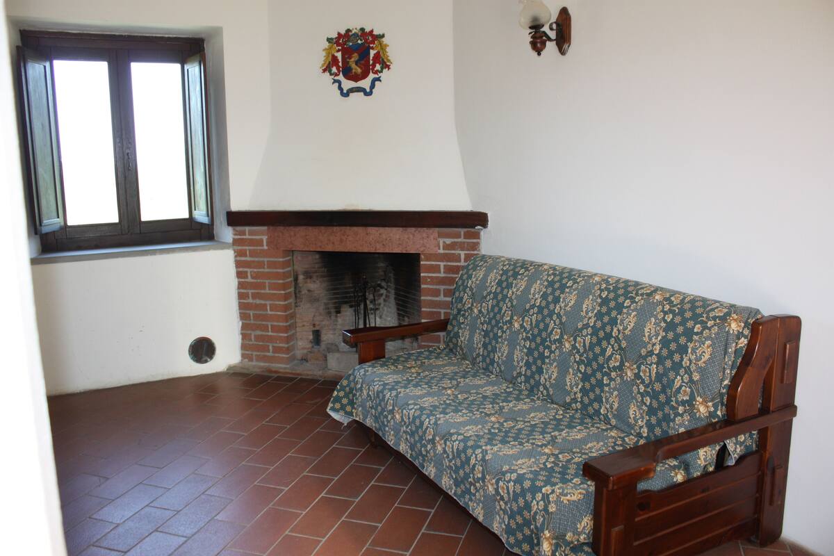 Ein Zimmer mit einem Kamin aus Ziegelsteinen, einer Couch und einem Fenster mit geöffneten Klappläden.