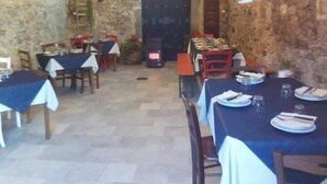 Un coin repas rustique avec des murs en pierre, des tables recouvertes de nappes blanches et des chaises.